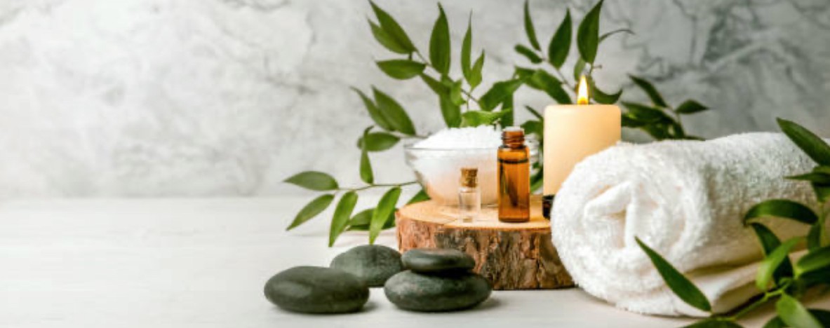 Spa essentials arranged with towels, stones, greenery, and candlelight.